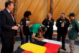 Man signing documents. Five people looking on.