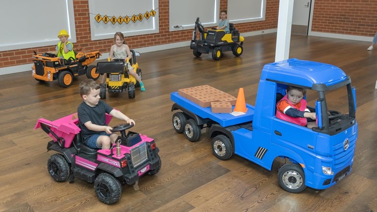 Children driving replica trucks and earthmovers.